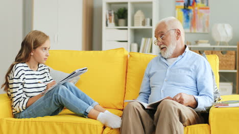 Senior-grey-haired-grandpa-helping-his-lovely-teenage-granddaughter-doing-her-homework.-At-home.